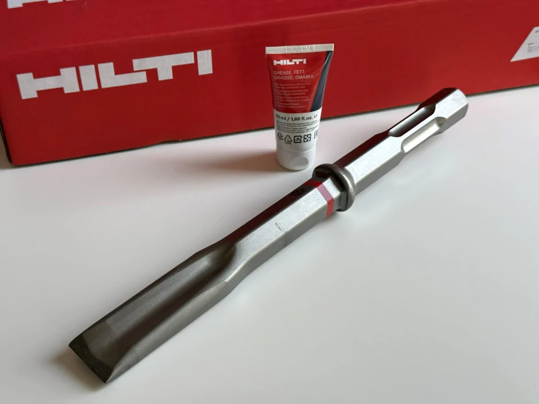 Burin plat Hilti TE-HX FM 40 à côté de son emballage rouge et d’un tube de graisse pour emmanchement